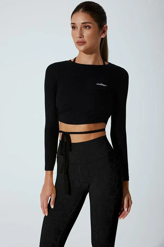 Woman wearing black long sleeve crop top with wrap detail and high-waisted leggings
