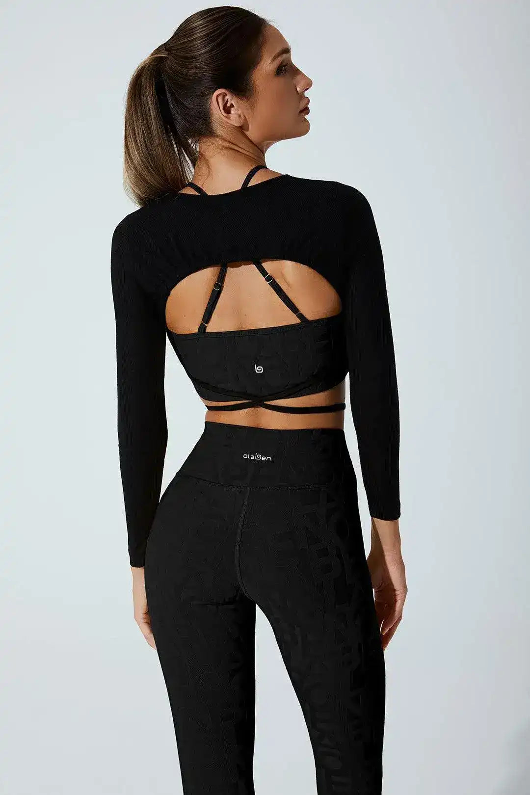 Woman modeling black long sleeve activewear top with open back and matching high-waisted leggings