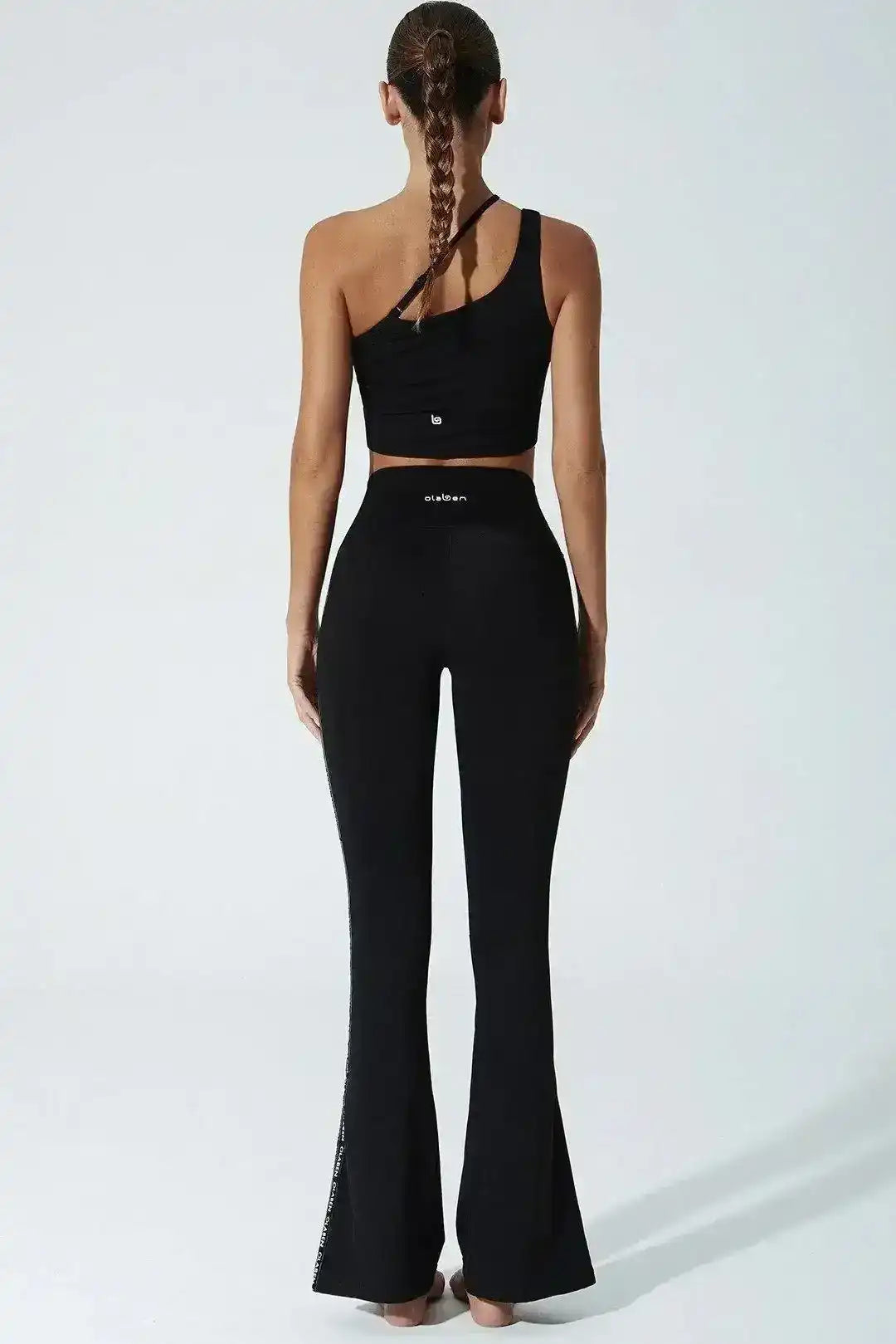 Woman wearing a black one-shoulder sports bra and high-waisted flare leggings, back view