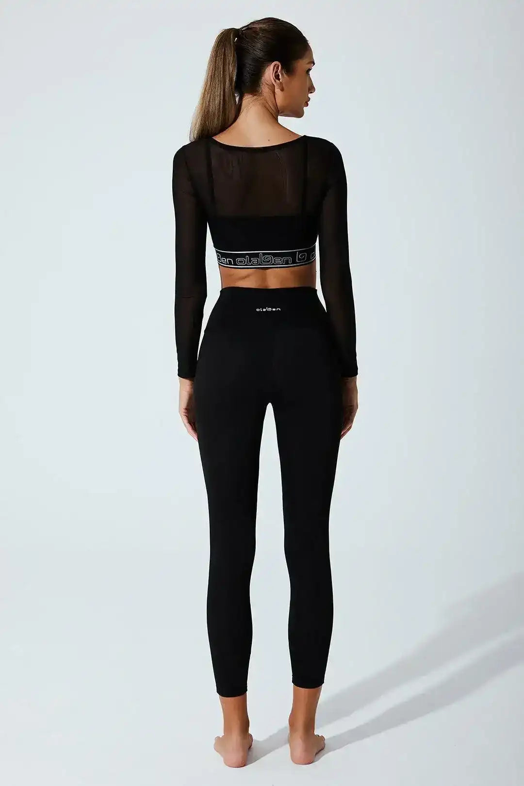 Woman in black long sleeve mesh crop top and high-waisted black leggings, back view