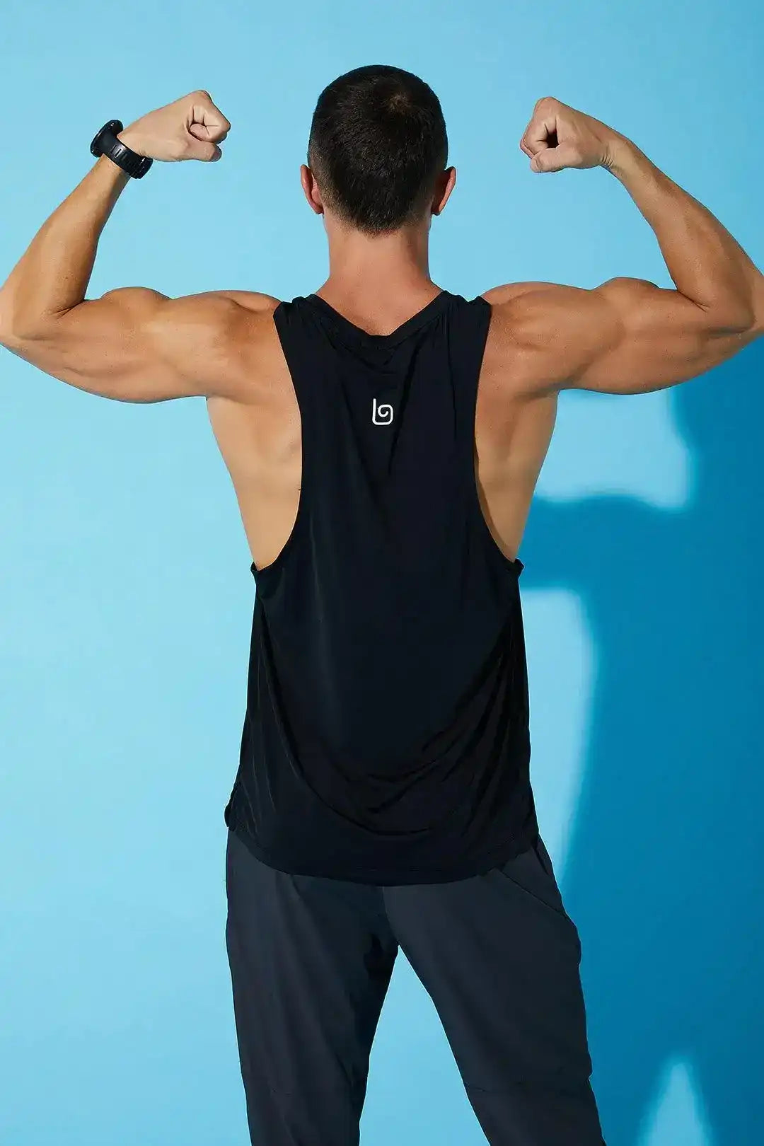 Man flexing in black athletic tank top and pants, blue background, activewear photo