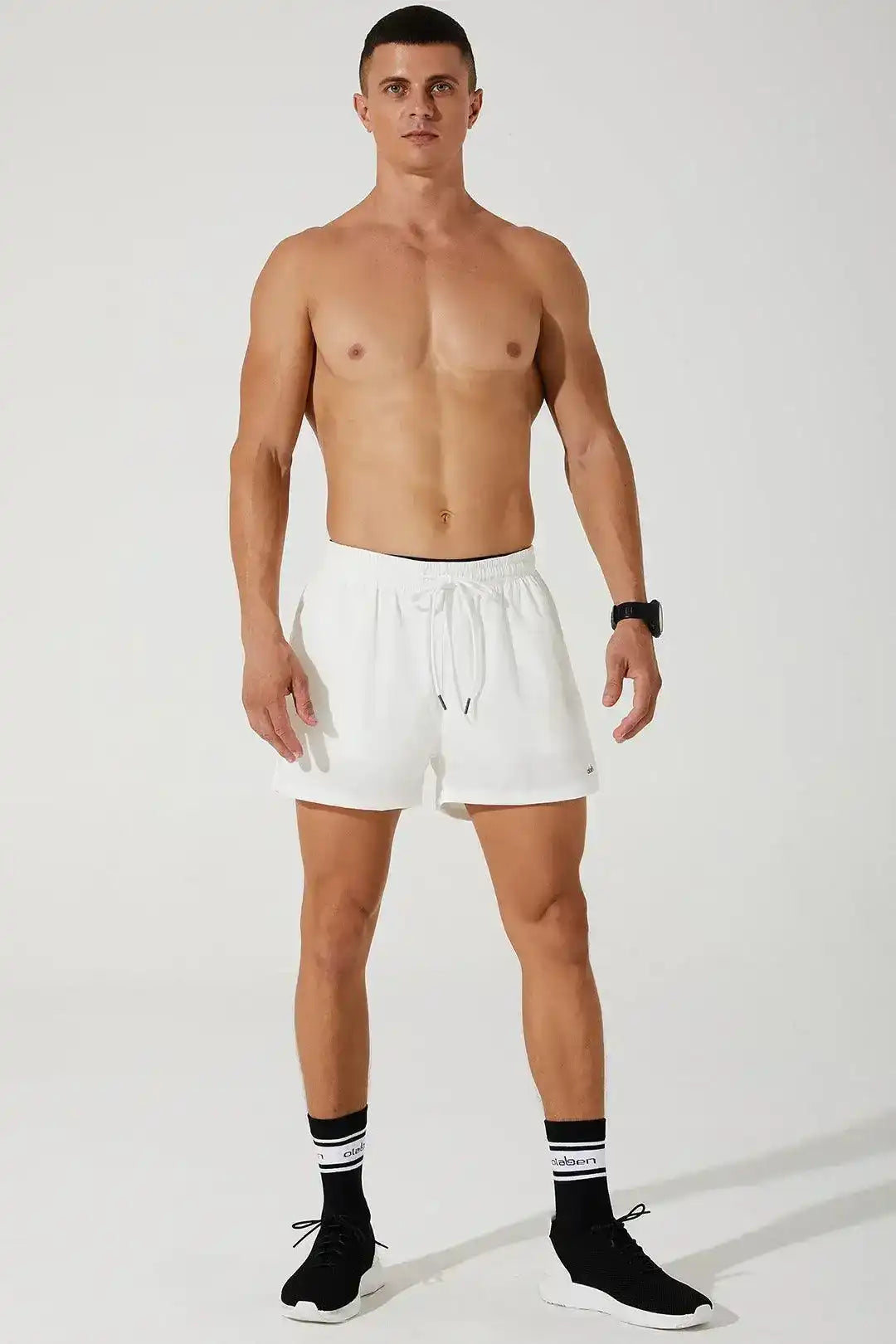 Man wearing white men's running shorts, black sneakers, and athletic socks, studio setting