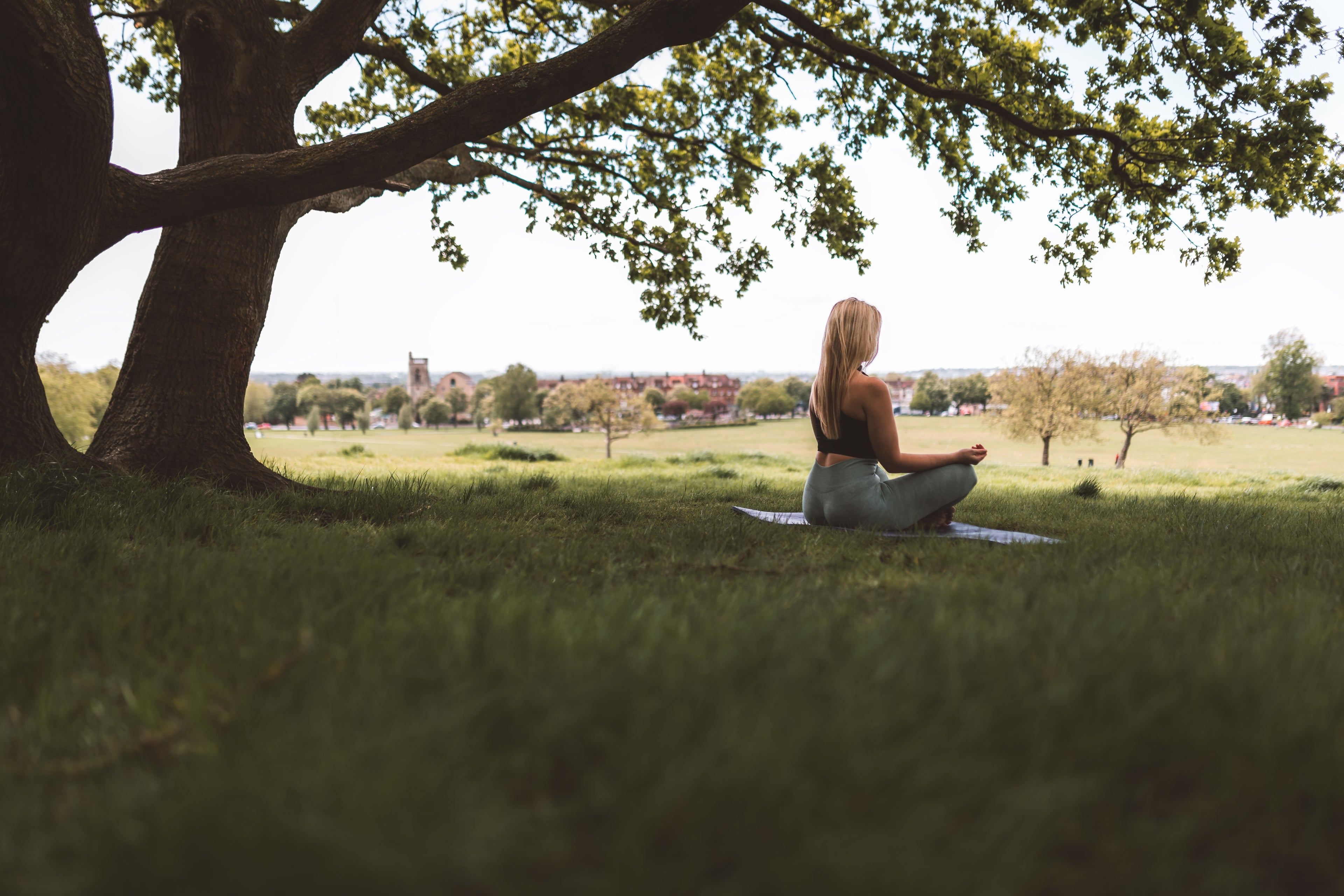 woman-sits-under-large-tree-on-a-yoga-mat - Olaben