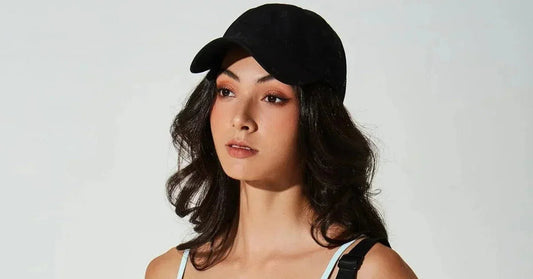 Woman wearing a black baseball cap and white activewear top against a light background