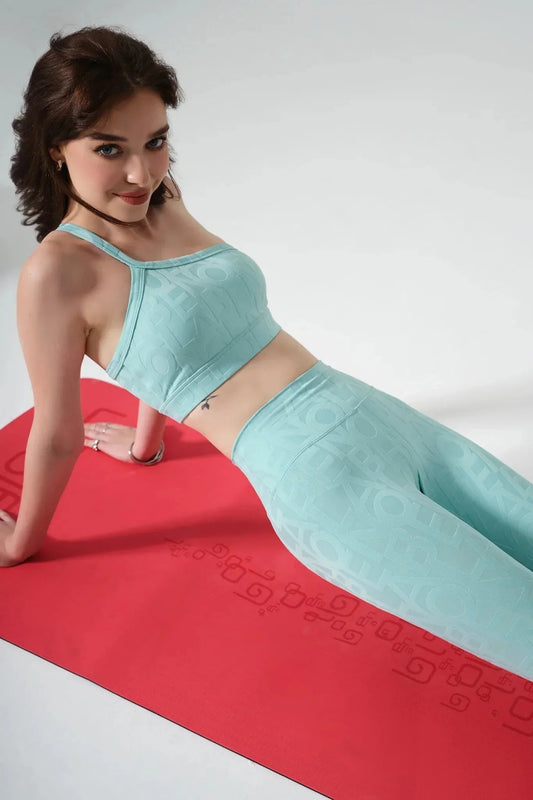 Woman in light blue seamless activewear set doing yoga pose on a red mat