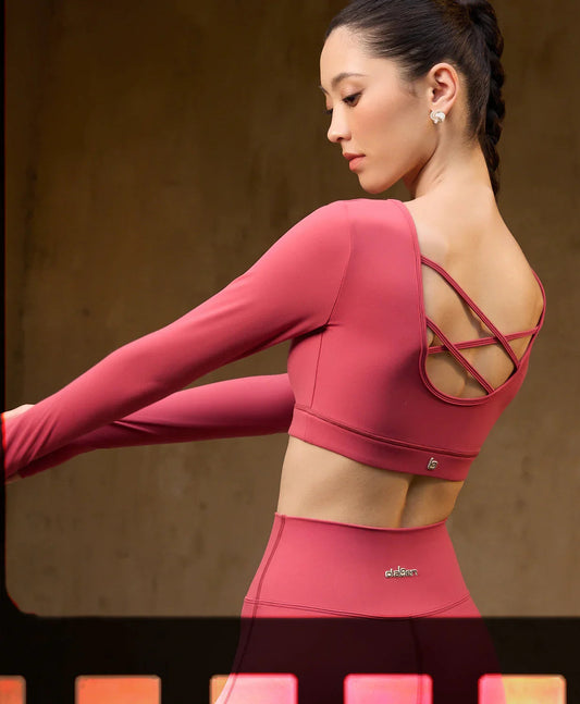 Woman in pink long sleeve activewear set with strappy back design, stretching indoors