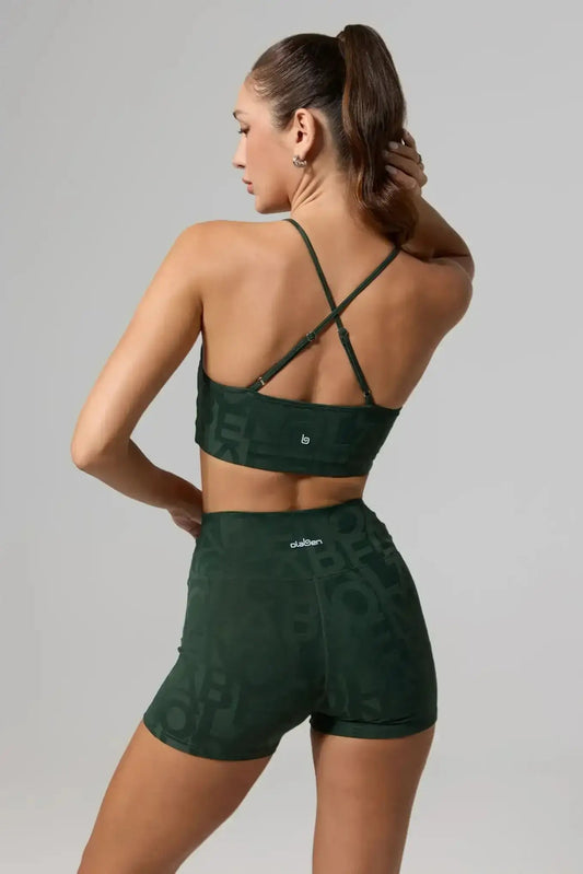 Woman wearing olive green strappy sports bra and high-waisted shorts, back view