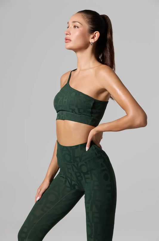 Woman wearing an olive green one-shoulder sports bra and matching high-waist leggings