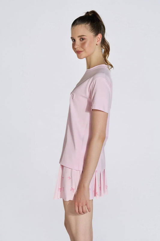 Woman in pink embossed logo t-shirt and pleated skirt, side view, white background