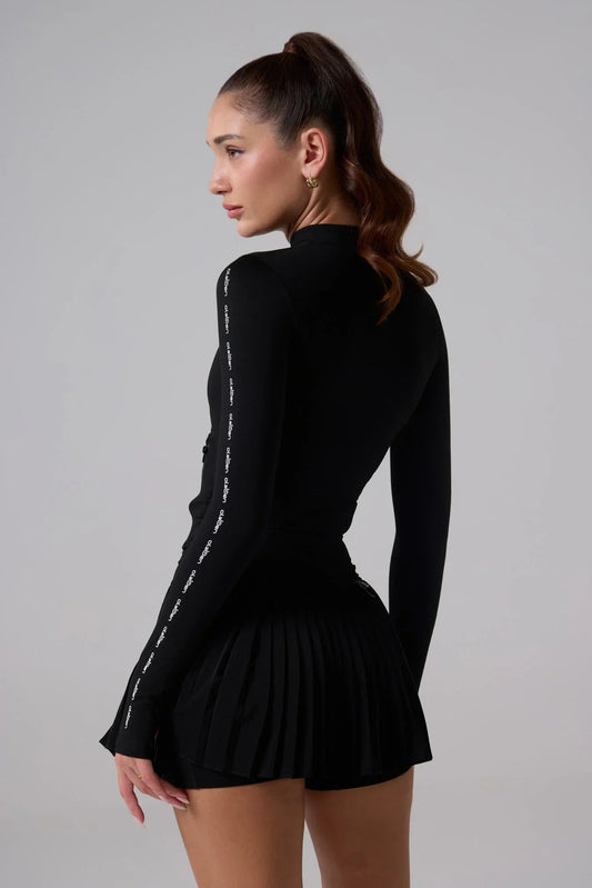 Woman wearing black fitted athletic jacket with long sleeves and pleated skirt, back view
