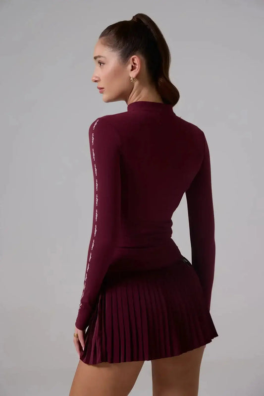 Woman modeling a dark red long sleeve athletic jacket and pleated skirt, side view