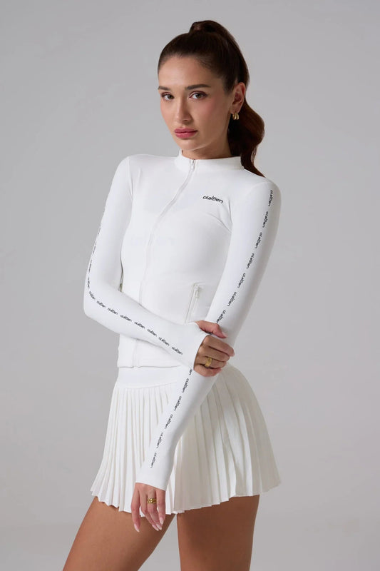 Woman wearing a white zip-up activewear jacket with logo details and a pleated skirt