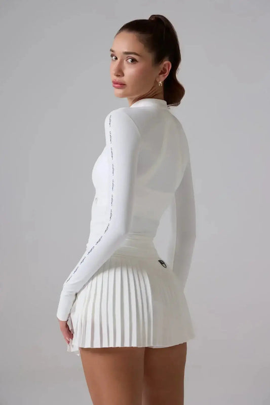 Woman wearing white long sleeve athletic top and pleated tennis skirt