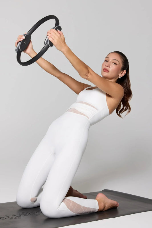 Woman in white jumpsuit doing Pilates on mat with fitness ring