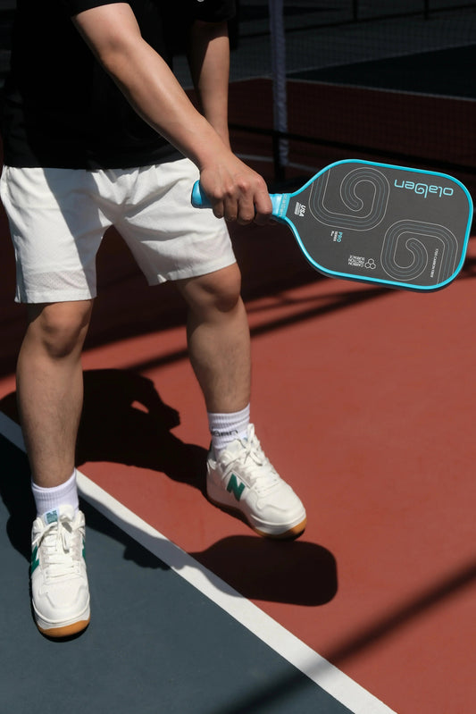 Person holding blue 16mm pro series pickleball paddle on outdoor court