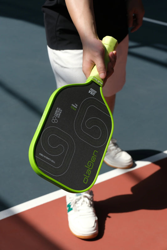 Person holding green edge pickleball paddle with black carbon fiber face on court