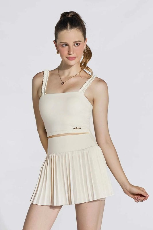 Woman wearing ivory ruffle strap crop top and pleated high-waist skirt, studio background
