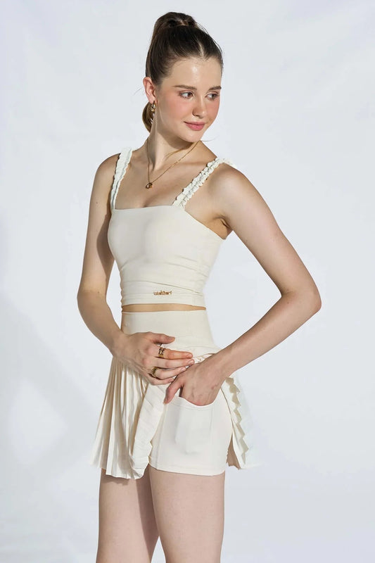 Woman wearing ivory white ruffle strap sports bra and matching pleated skirt with shorts