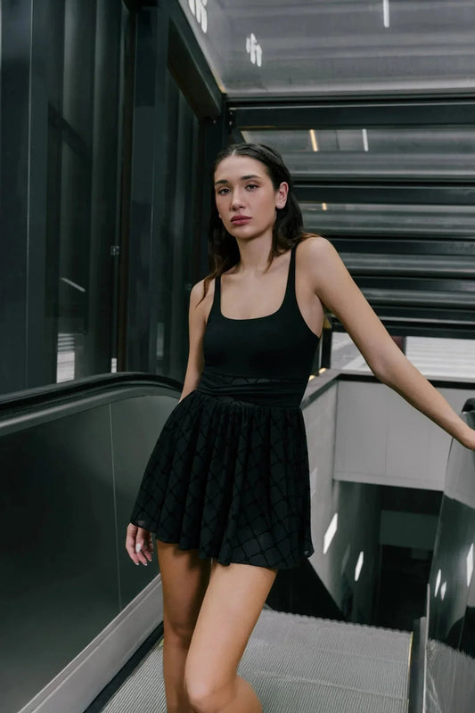 Woman in black sleeveless monogram dress standing on an escalator, modern indoor setting