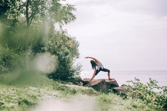 Woman practicing yoga pose on seaside rocks in activewear, surrounded by greenery