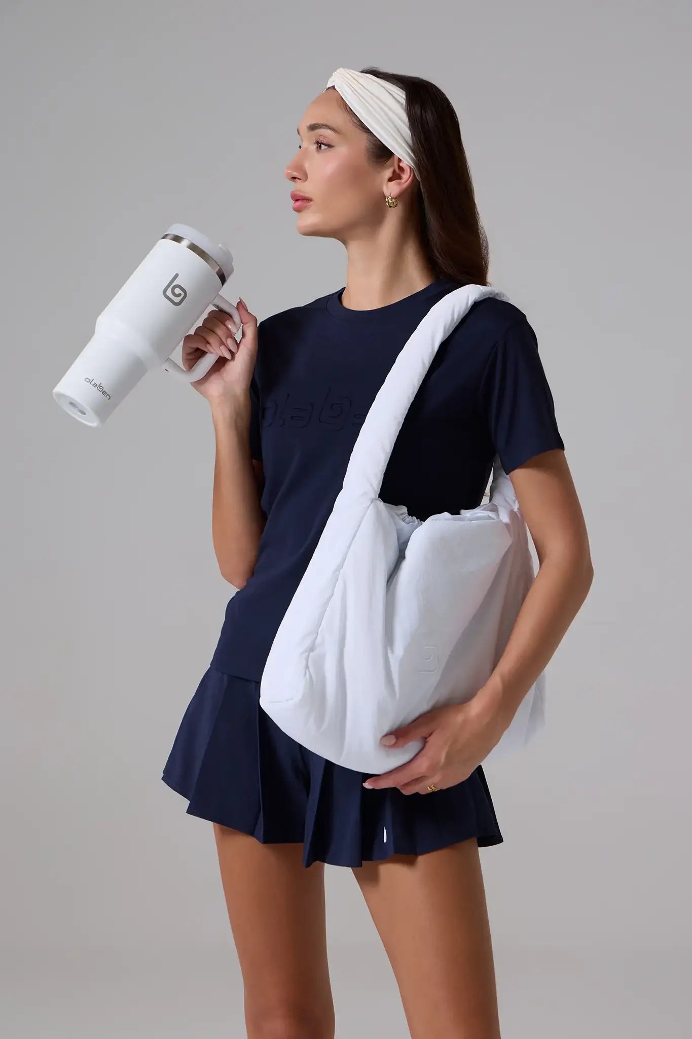 Woman in navy activewear holding white tumbler and carrying gym bag, ready for fitness or yoga